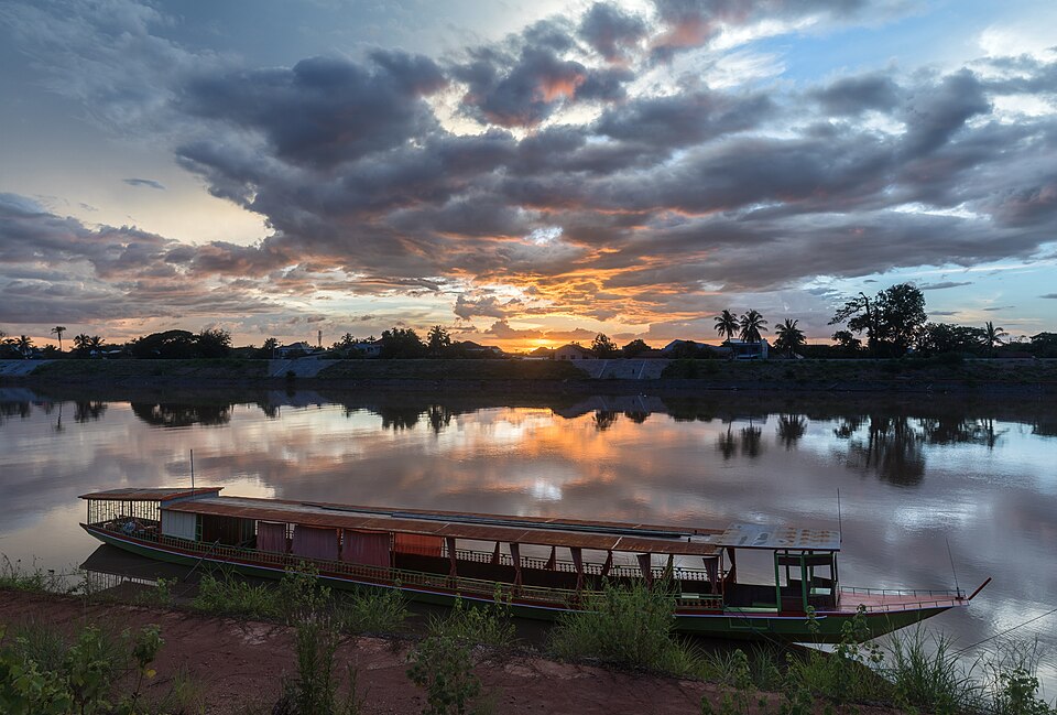 Water reflection of sunset with gray and orange clouds and a boat moored to the bank in Pakse Laos